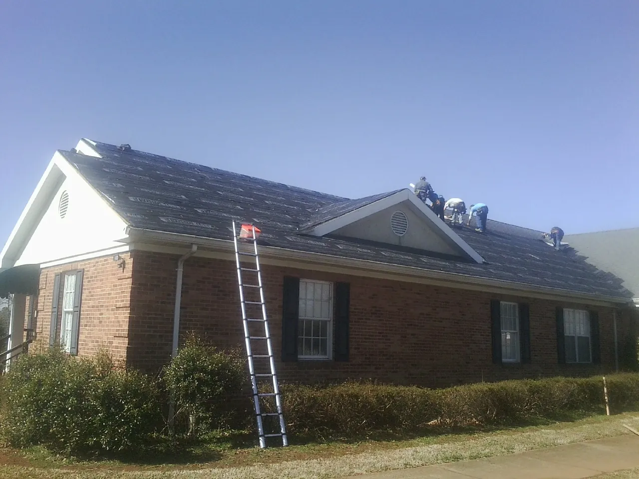 Crew tearing shingles off a brick ranch roof with a ladder set — Emergency Roof Repair work by our crew in Covina