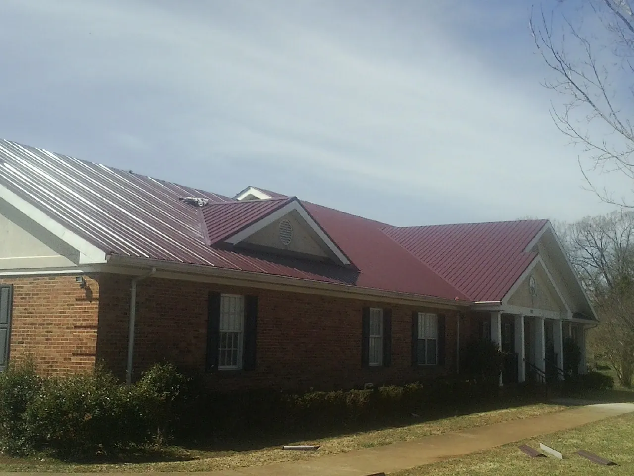 Red metal roof with gabled entries on a long brick building, from a Hail Damage Roof Repair job in Covina