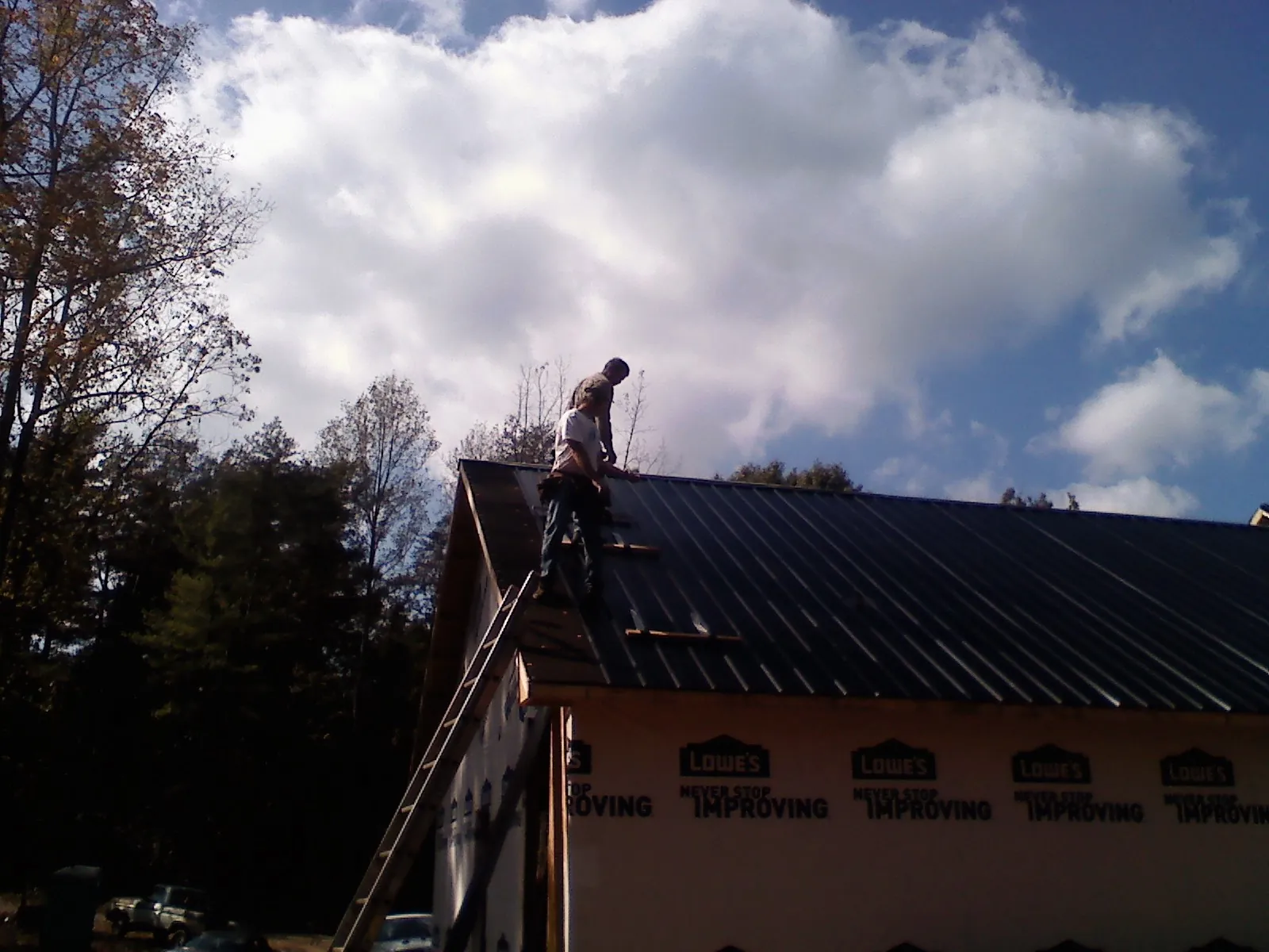 Roofer fastening dark metal panels high against a cloudy sky, from a Roof Inspection job in Covina